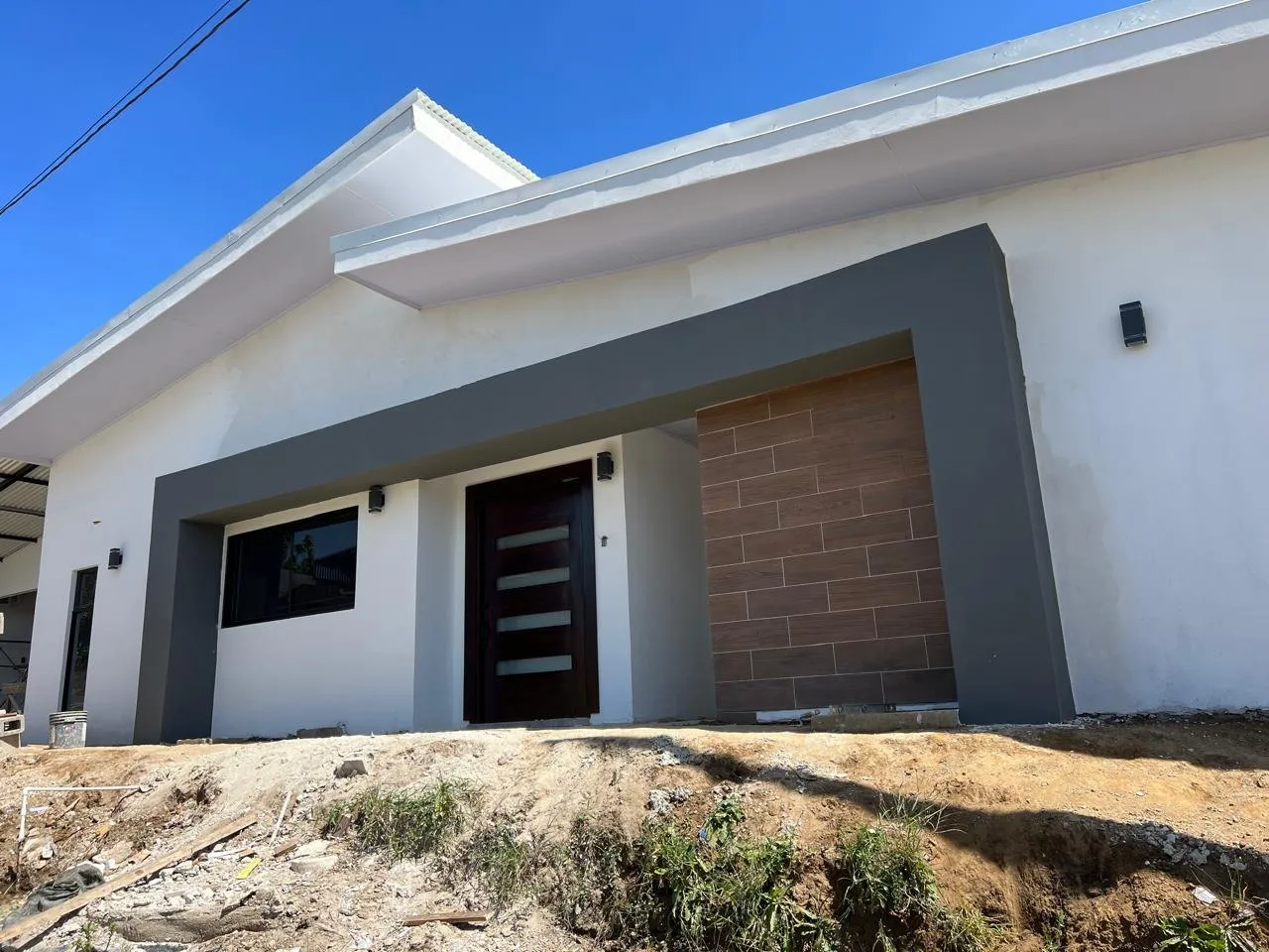 Residencia de una planta con techo inclinado, marco gris en la fachada y puerta de madera.